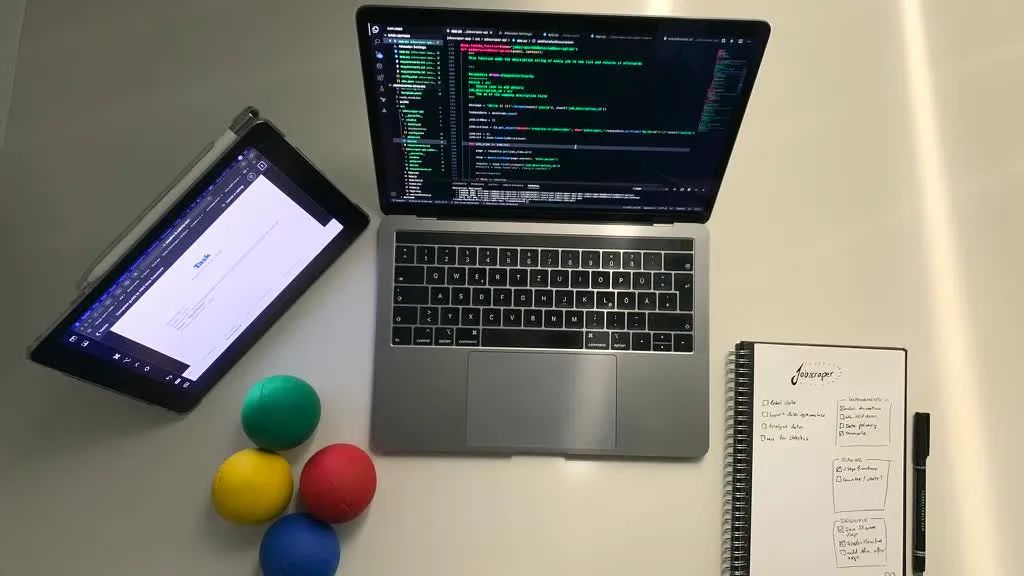 Overhead view of a desk showing a laptop with code on screen and juggling balls resting nearby