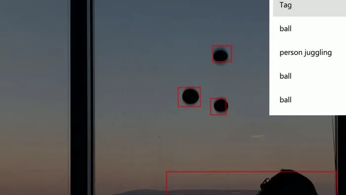 A juggler mid-throw in front of a window, with Azure Custom Vision bounding boxes visible around the body and ball in the detection overlay