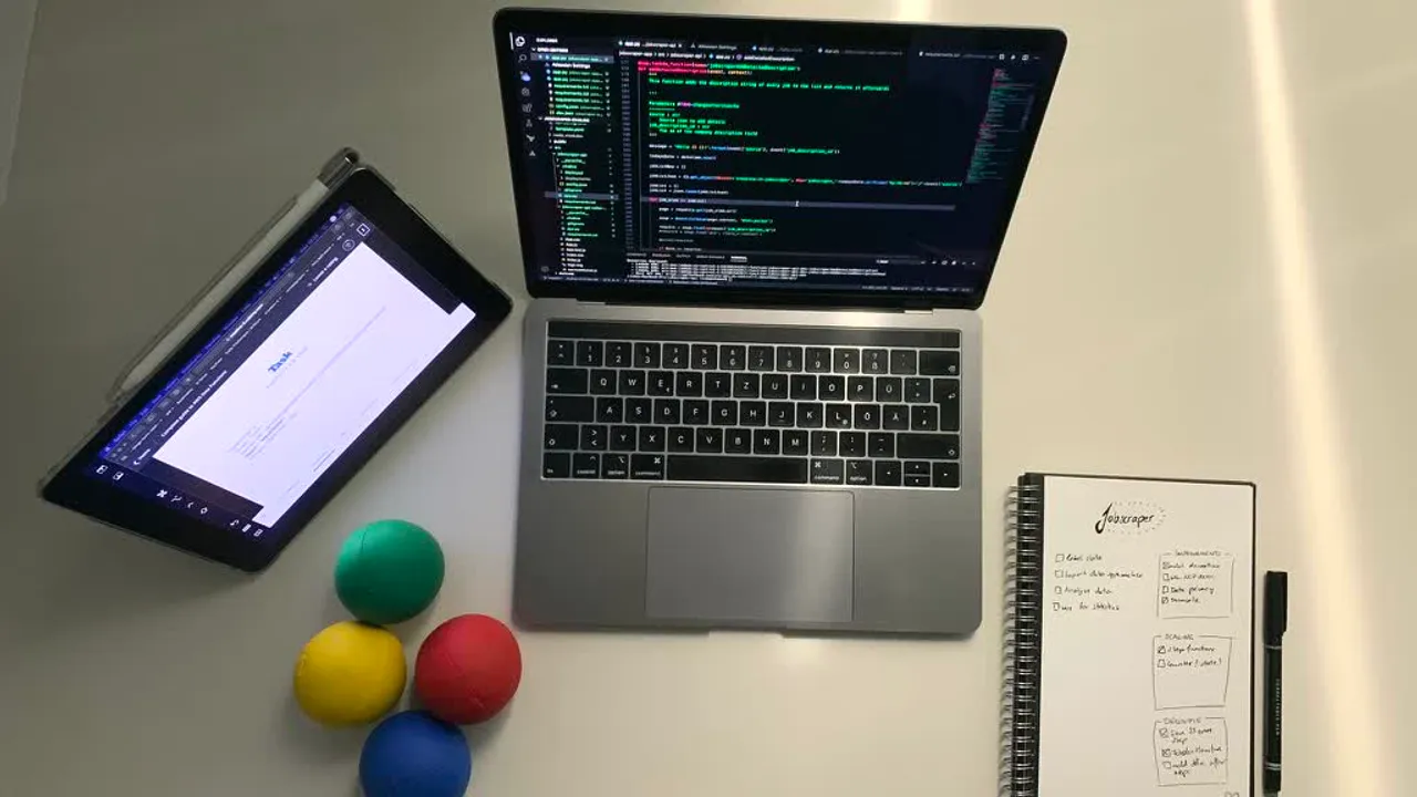 Overhead view of a desk showing a laptop with code on screen and juggling balls resting nearby