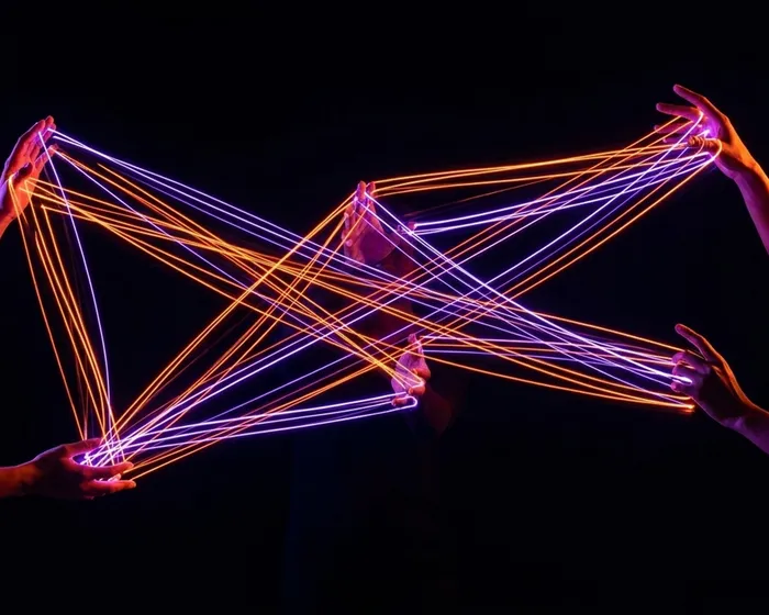 Hands holding neon strings in a cat's cradle formation, showing interconnected dependencies
