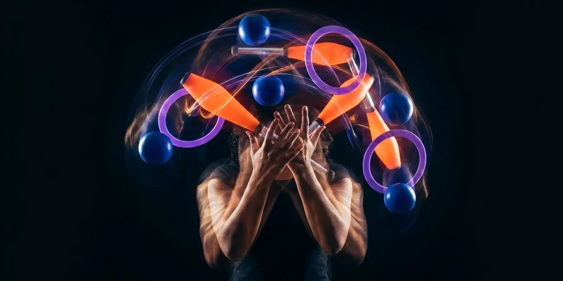 Juggler in motion blur with all three props - balls, clubs, and rings - simultaneously in the air