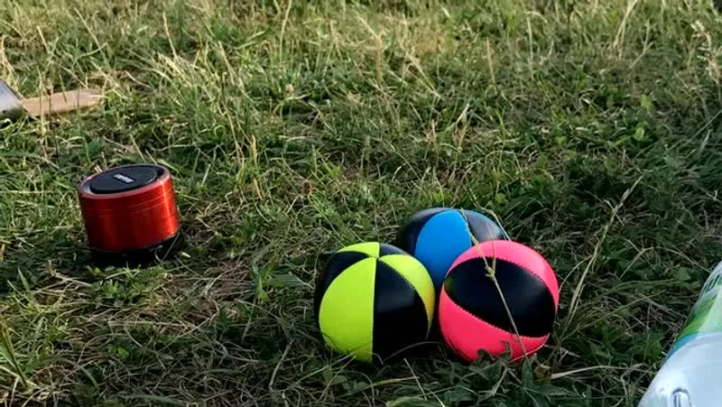 Three neon juggling balls resting in green grass, bright colors against the natural ground