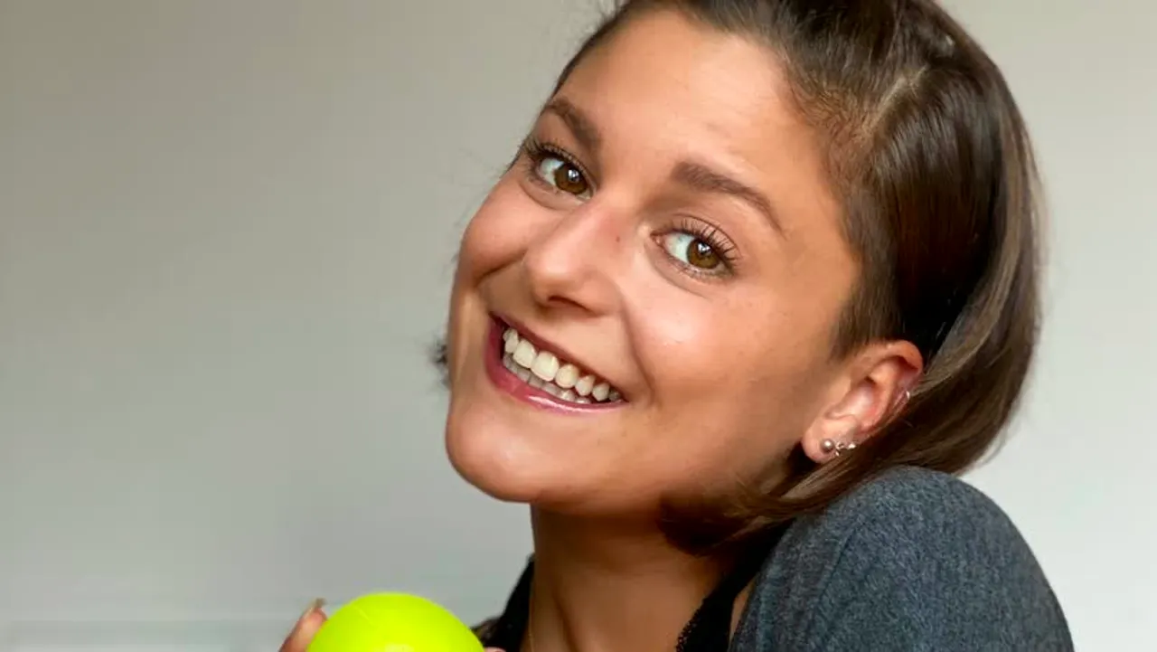 A juggler smiling while keeping three neon balls in the air, face showing delight rather than concentration